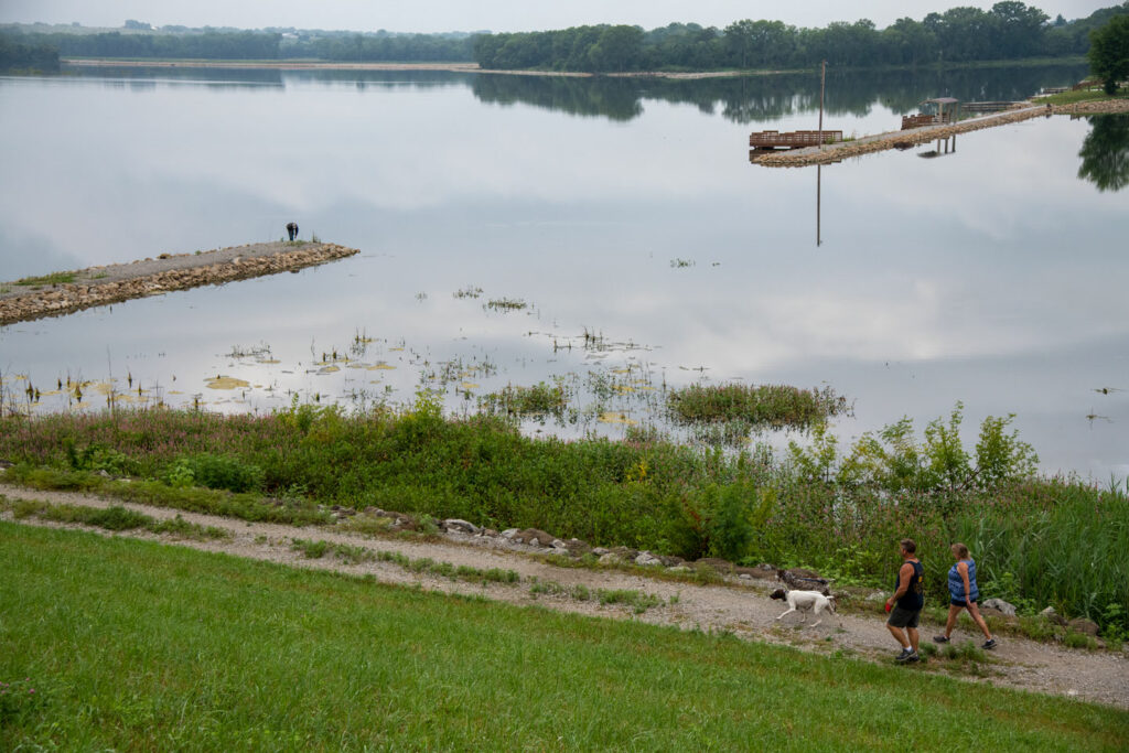 Two people walk along a lake with their dog