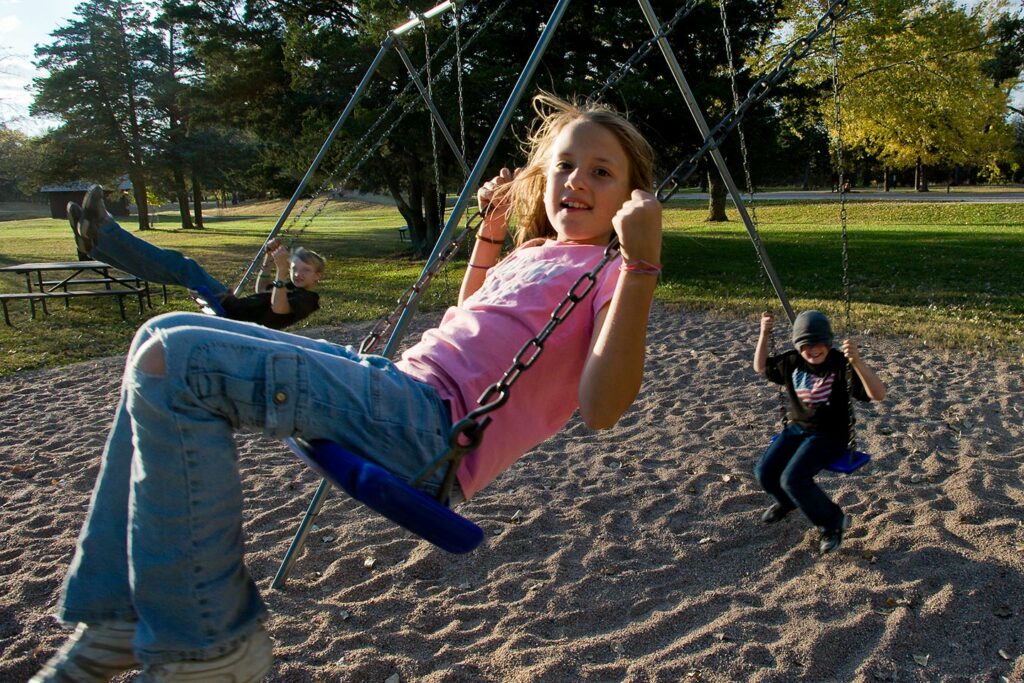 Three smiling kids swing on a swingset