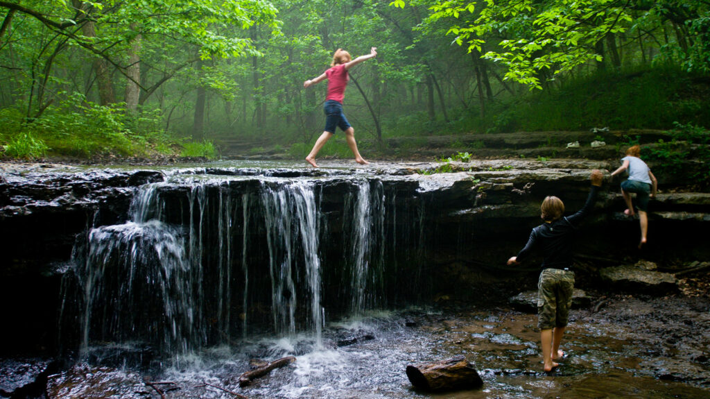 children play in a shallow waterfall in the creek