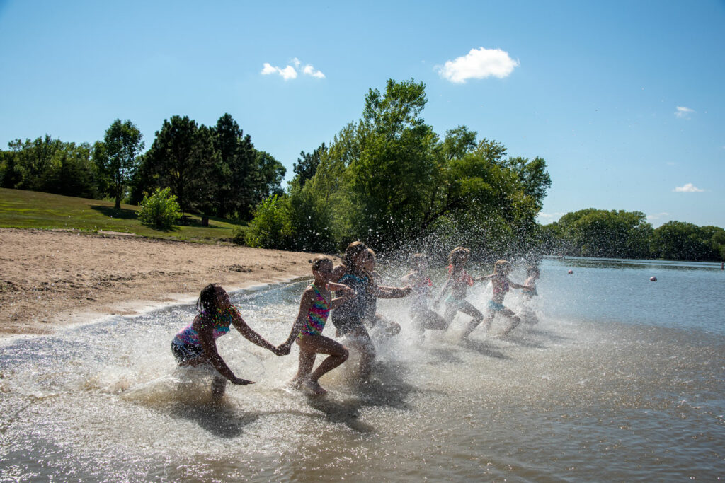 A set of young girls runs into the water from the beach while holding hands.