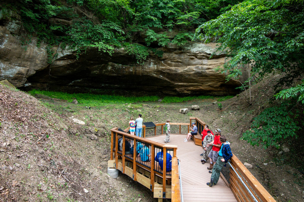 viewed from the boardwalk, park goers sit on benches on a boardwalk, looking into the cave