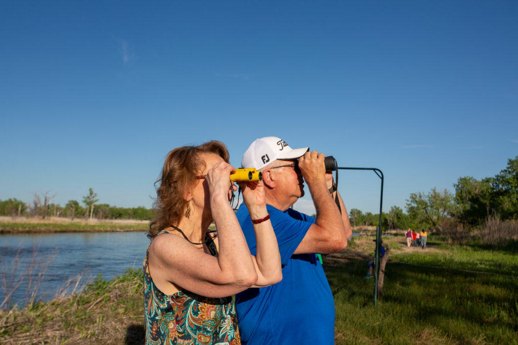 A man and woman look through their binoculars.