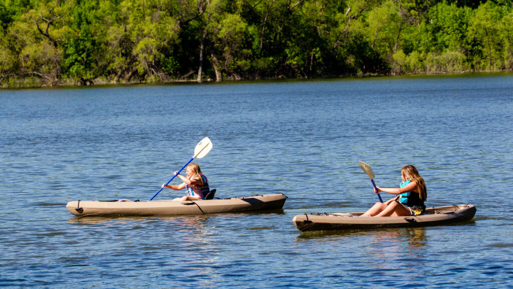 two young girls paddle in kayaks on the lake on a sunny day