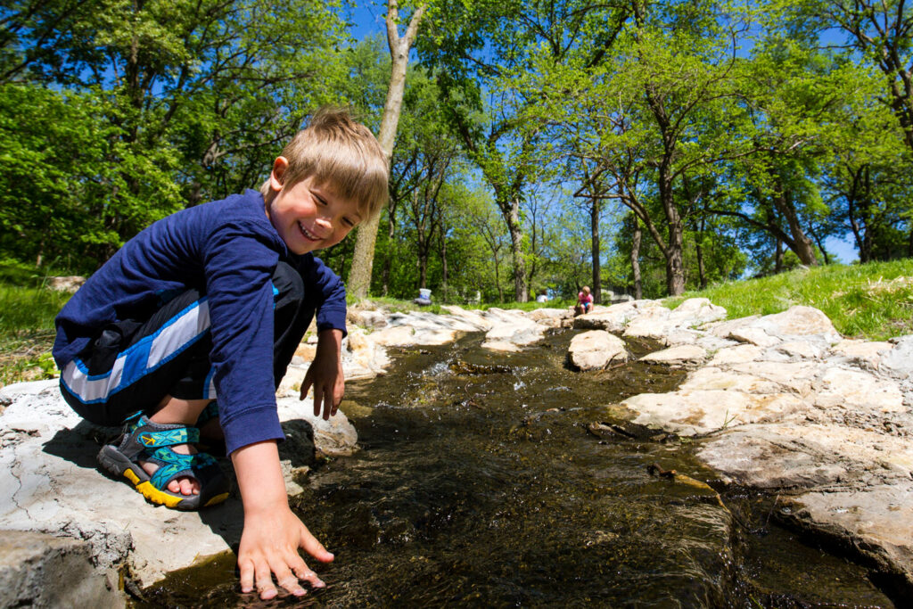 a smiling young boy gets his hands dirty playing in the interactive stream