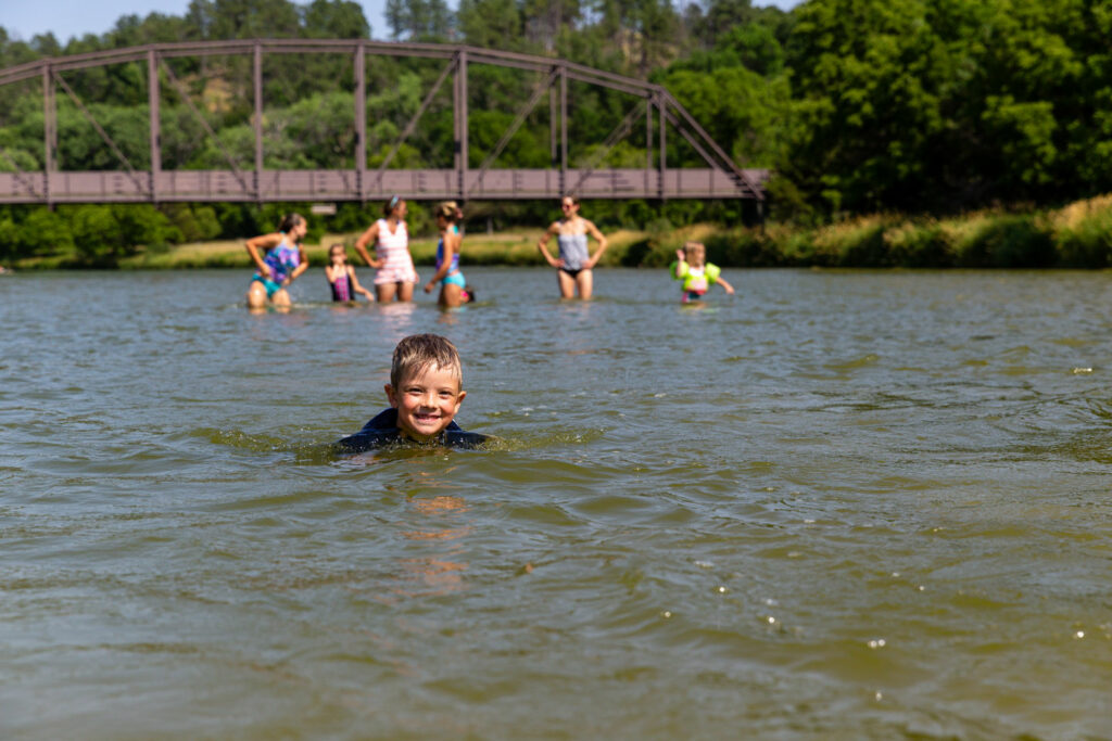 A boy, grinning at the camera, floats on his belly in a river