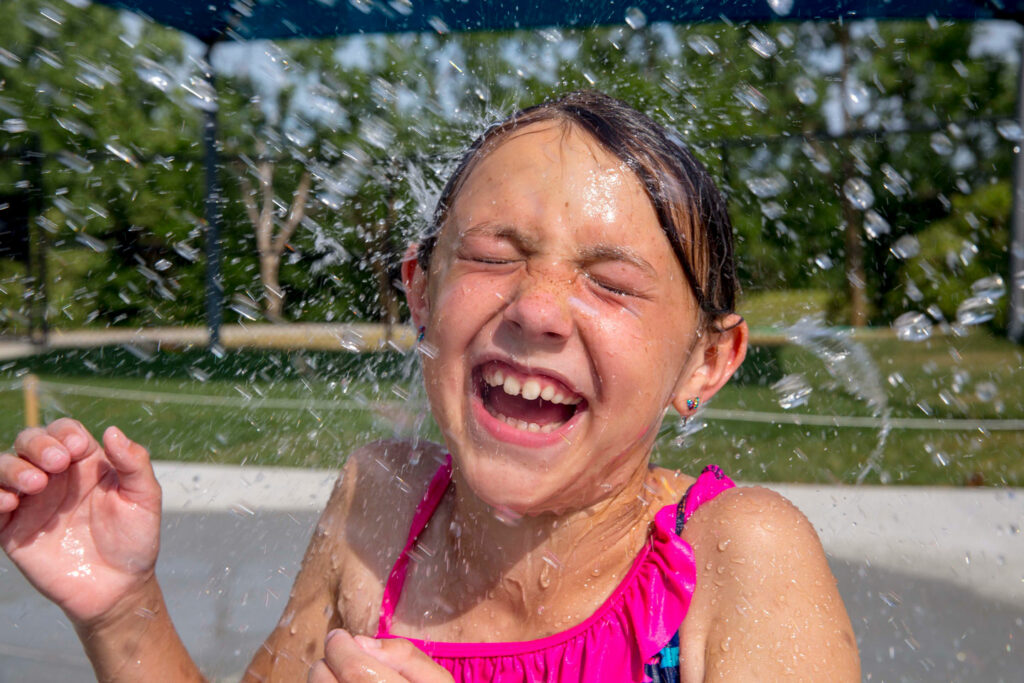 closeup of a young girl in a swimsuit laughing while being splashed with water