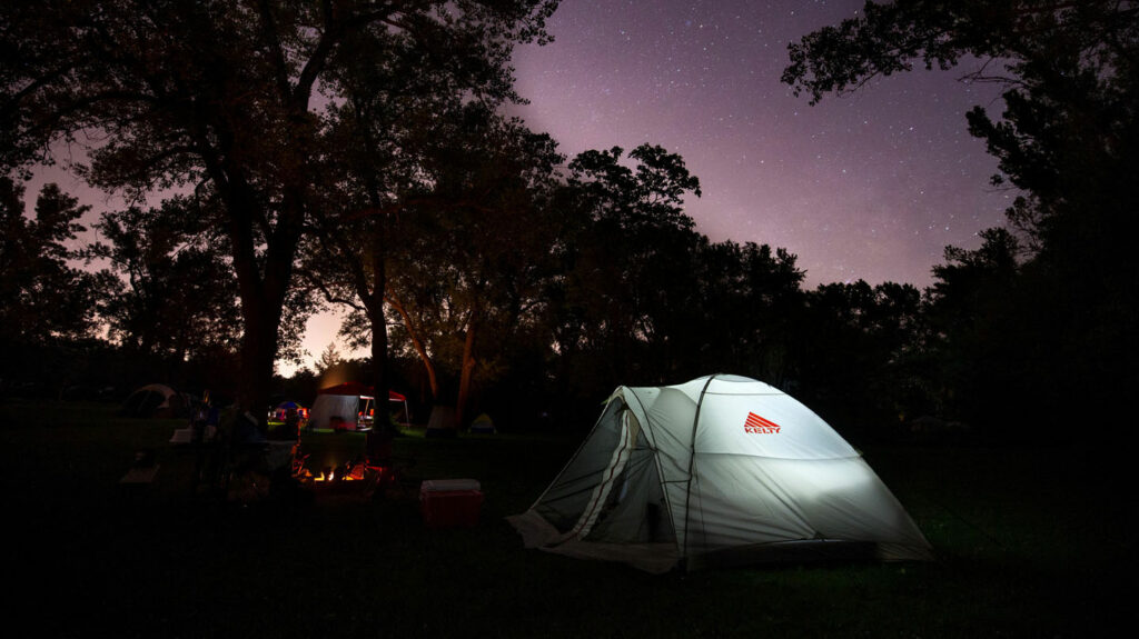 a tent is illuminated from the inside under a starry night sky