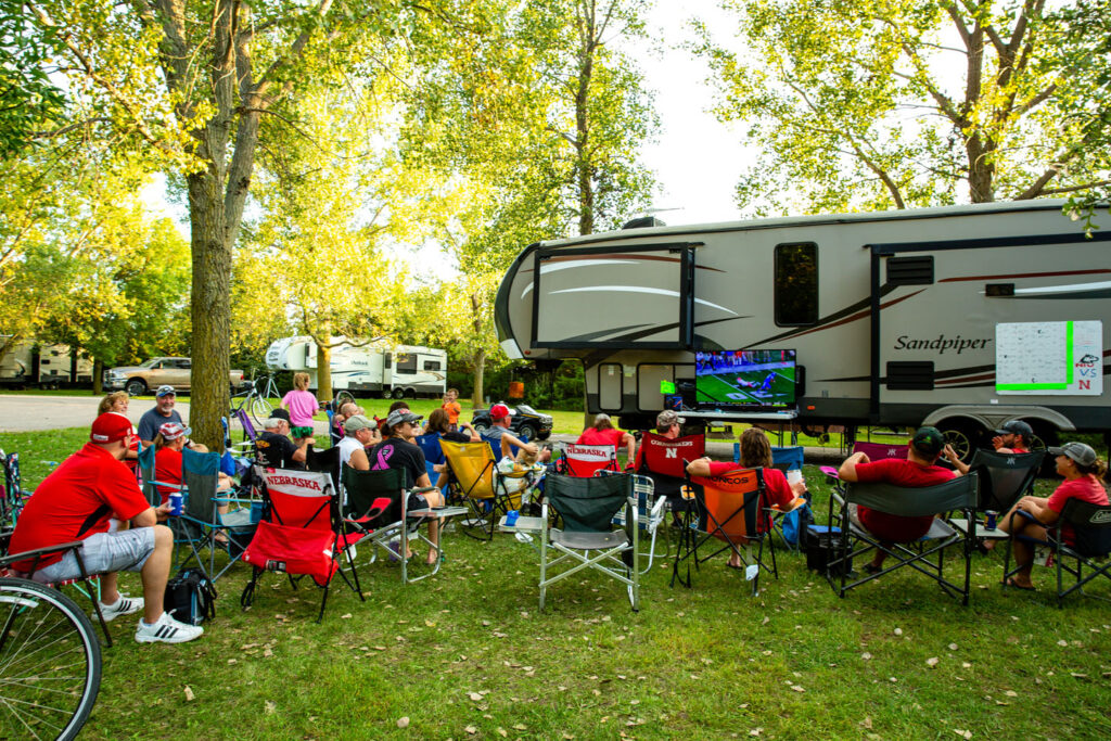 many people in camp chairs gather to watch a football game on a TV at an RV campsite