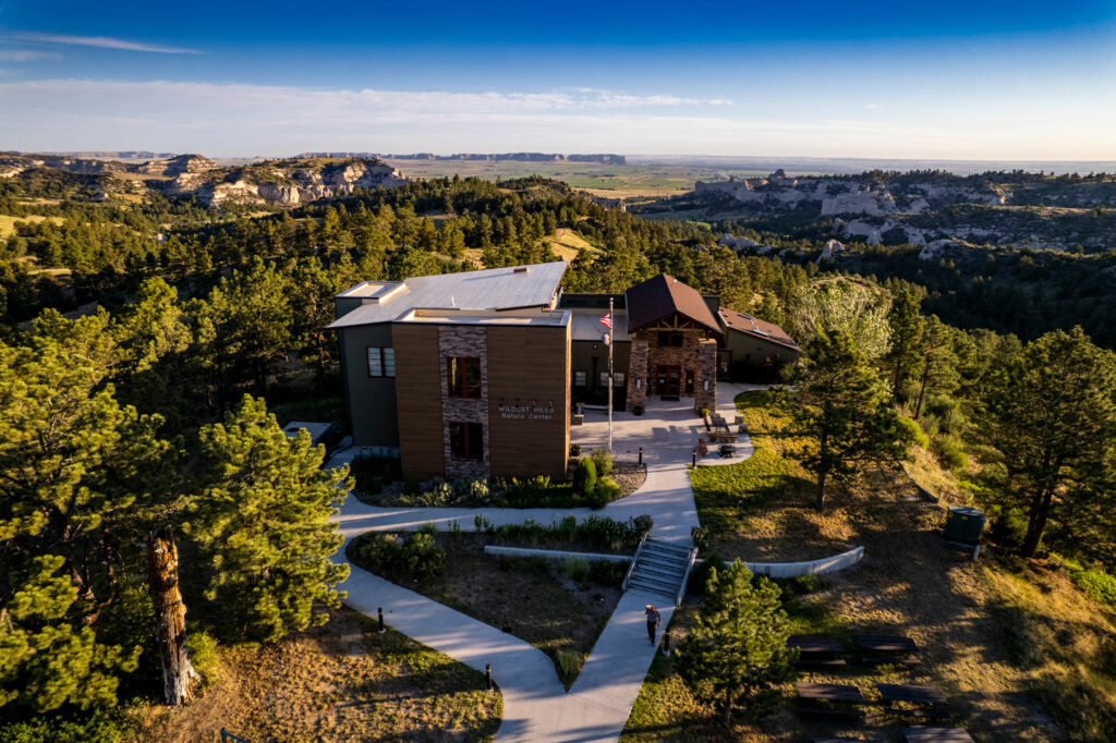 A sidewalk heads to the Wildcat Hills Nature Center, which surrounded by pine trees.