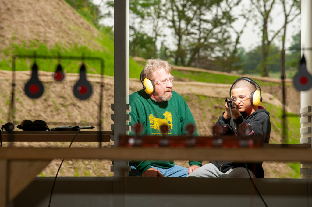 A man and his grandson use an airgun at a range.