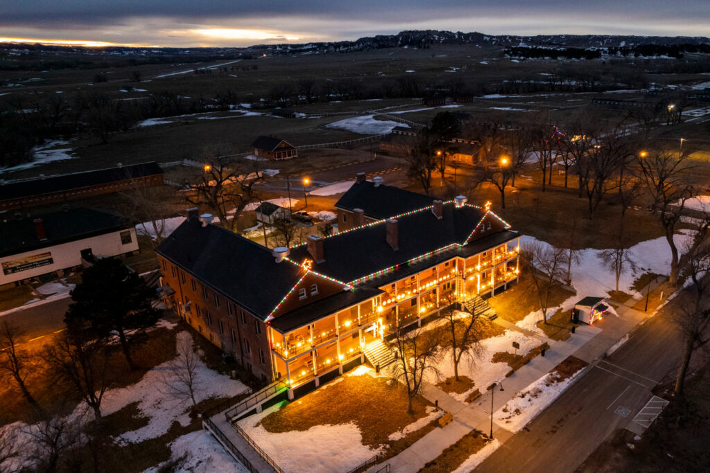 Fort Robinson's lodge decorated in Christmas lights glows under an evening sky