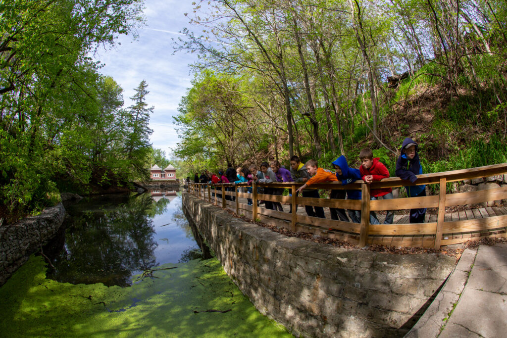 Children stand along a bridge by a pond