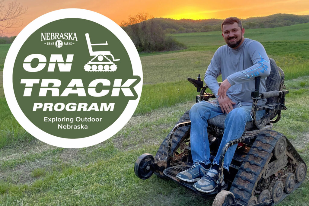 A man rides in an all-terrain track chair while outdoors with the sun setting in the background.