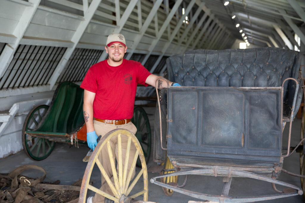 A park worker poses with a horse drawn buggy they are restoring at a state historical park.