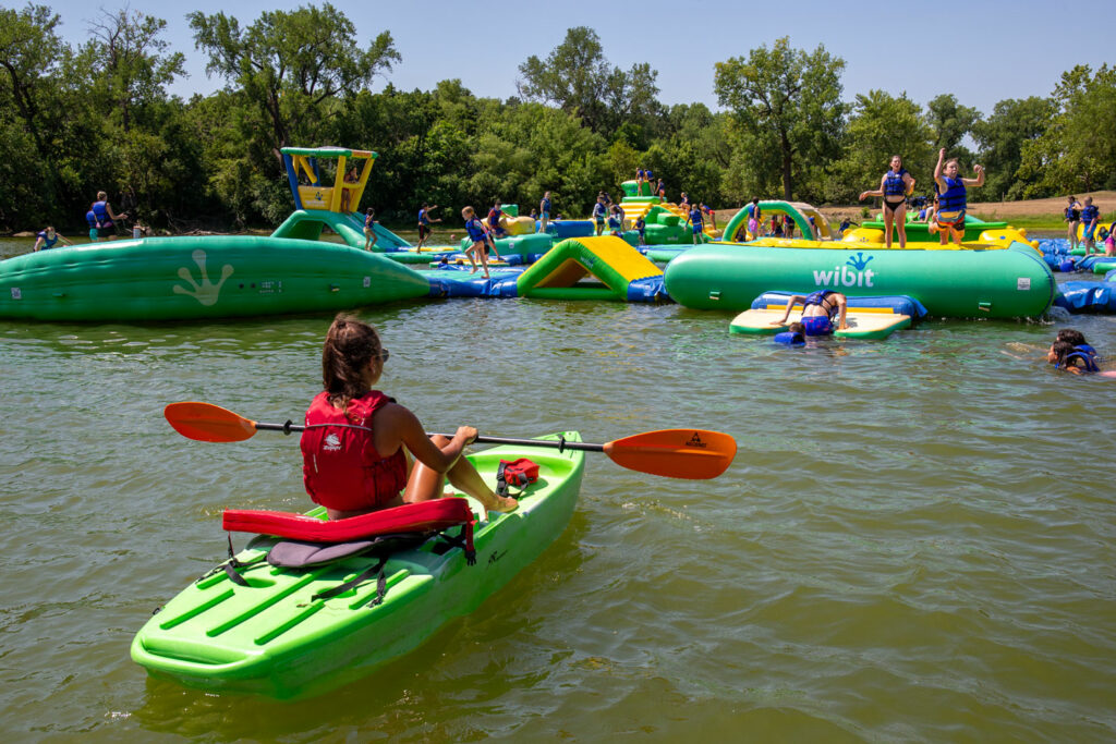 A lifeguard in a kayak oversees people swimming on a floating playground in a lake