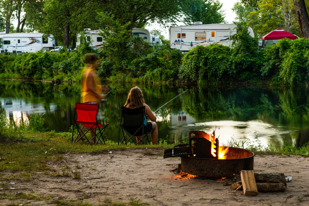 A boy and girl fish from their campsite at Fremont Lakes SRA near a campfire.